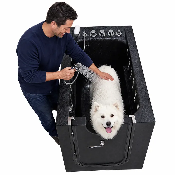 Man rinsing a fluffy white dog with the hand-held shower inside the pet tub